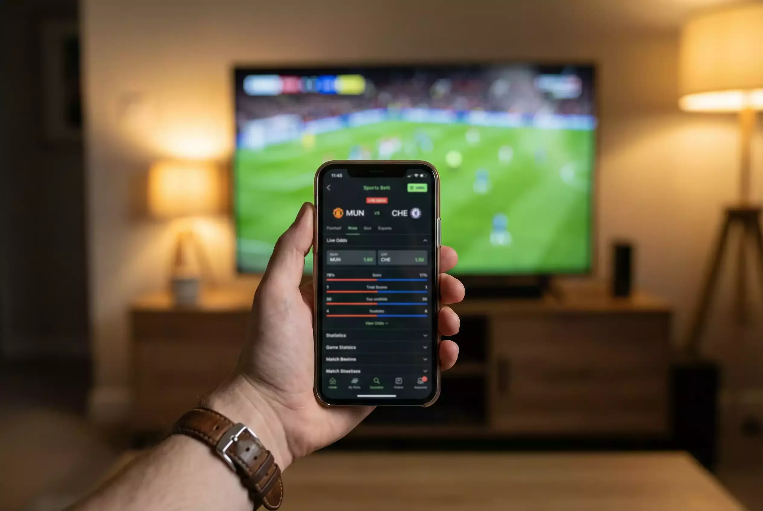 Hand hält Smartphone mit Sportwetten-App vor Fussballspiel im Hintergrund